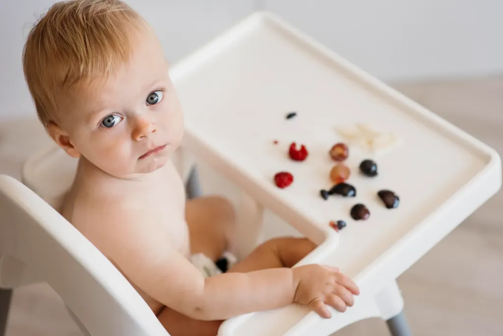 Criança está em uma cadeira de alimentação e mostra como a alergia alimentar em bebês é frequente.