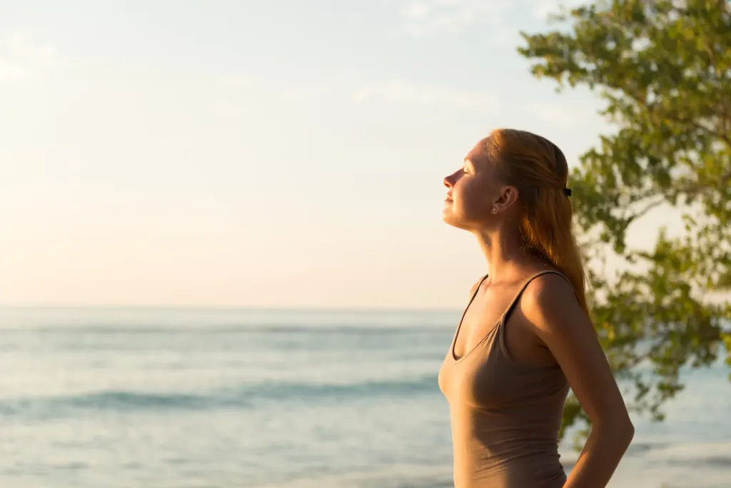 Mulher está numa praia sob o sol da manhã, Ela se expõe ao sol devido a carência de vitamina D.