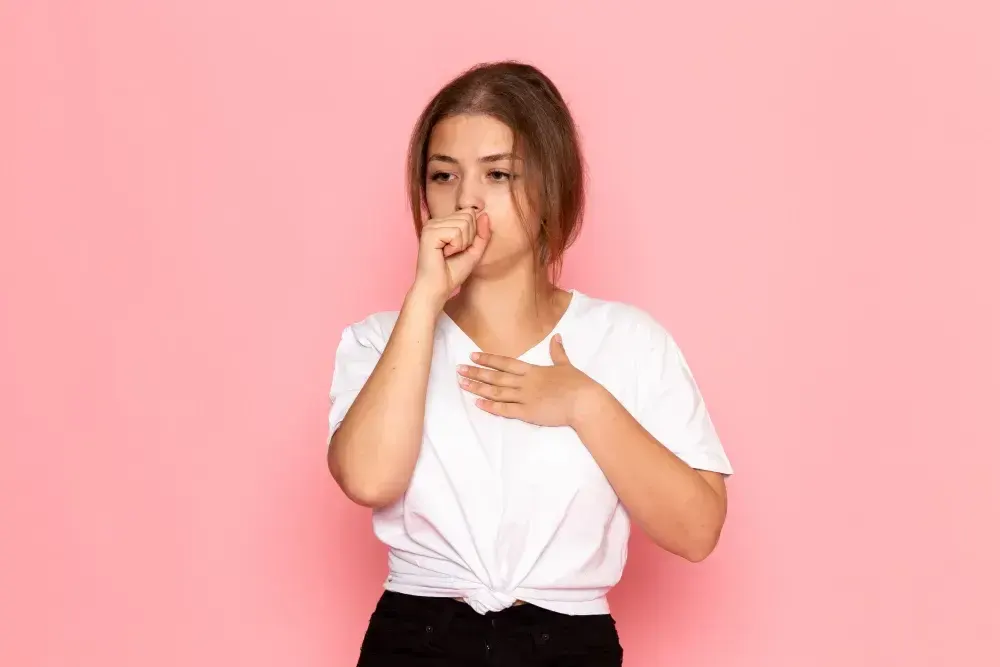 Mulher coloca uma mão abaixo do pescoço e outra leva à boca porque tem soluço.