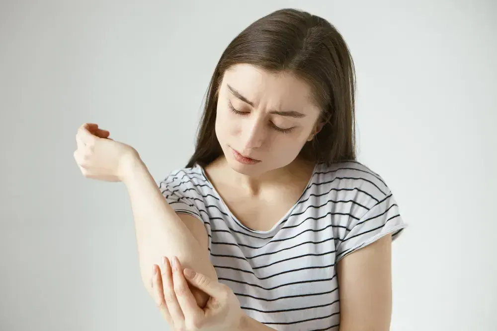 Mulher olha para o braço esquerdo e busca informações sobre escoliose tratamento.