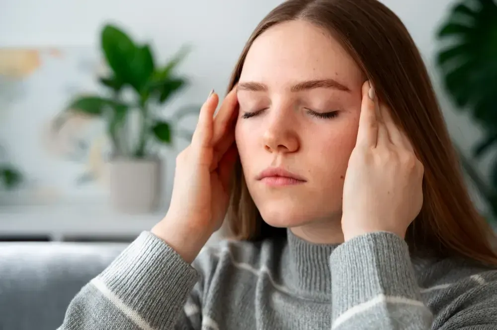 Mulher jovem coloca as mãos no rosto e tem sintomas de espasmo hemifacial.