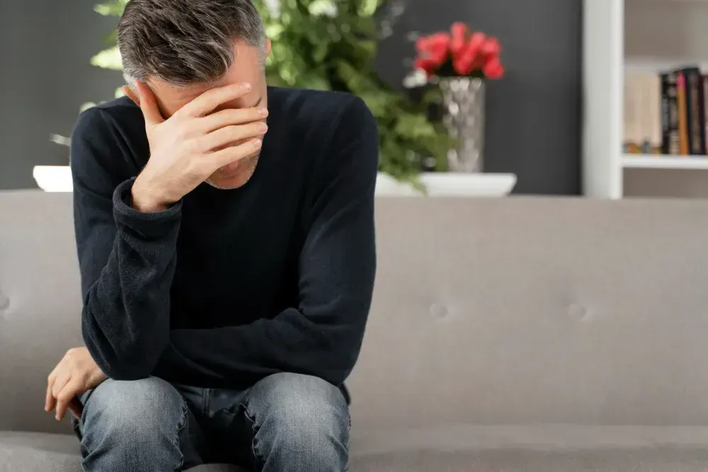 Homem está triste no sofá e apresenta sinais de depressão.